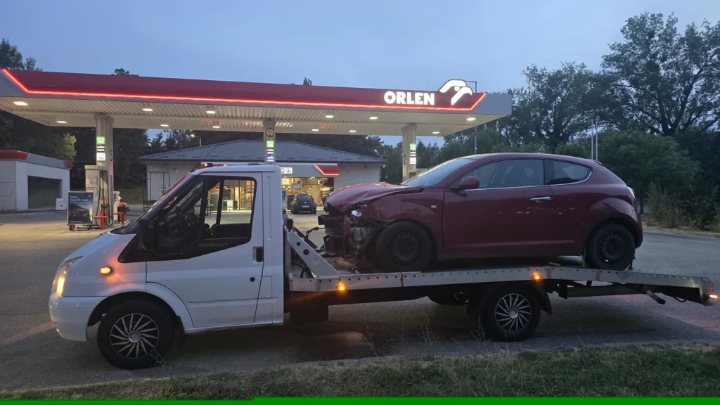 Frontálisan sérült Alfa Romeo MiTo a mentőautón egy benzinkútnál, alkonyatkor